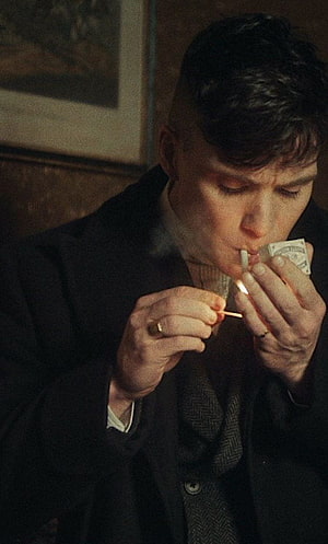 Cillian Murphy lighting a cigarette in a dimly lit room with vintage attire HD phone wallpaper
