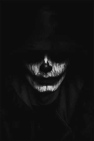 Monochrome Portrait of a Hooded Figure with Distressed Clown Face Paint in Deep Shadow HD phone wallpaper