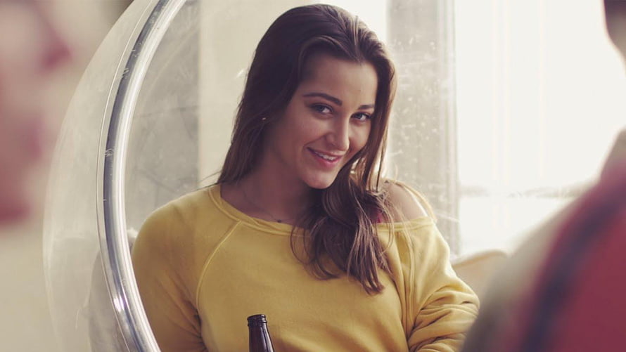 Daisy Ridley in a yellow sweater smiling warmly while holding a bottle in a cozy indoor setting HD wallpaper