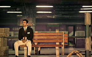 Sushant Singh Rajput as MS Dhoni in a formal suit sitting on a wooden bench at a train station platform HD wallpaper