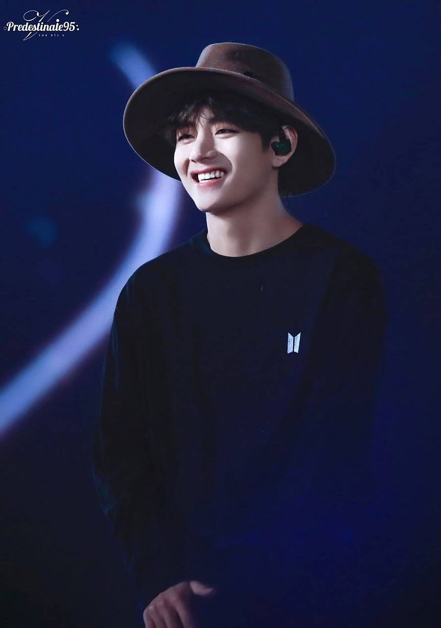 V from BTS smiling in a brown hat and black shirt on stage HD phone wallpaper