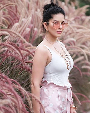 Sunny Leone posing in pink polka dot pants and white top amidst ornamental grass HD phone wallpaper