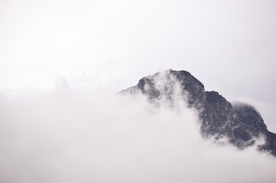 Minimalist mountain peak emerging from thick fog and clouds in a monochrome landscape HD wallpaper