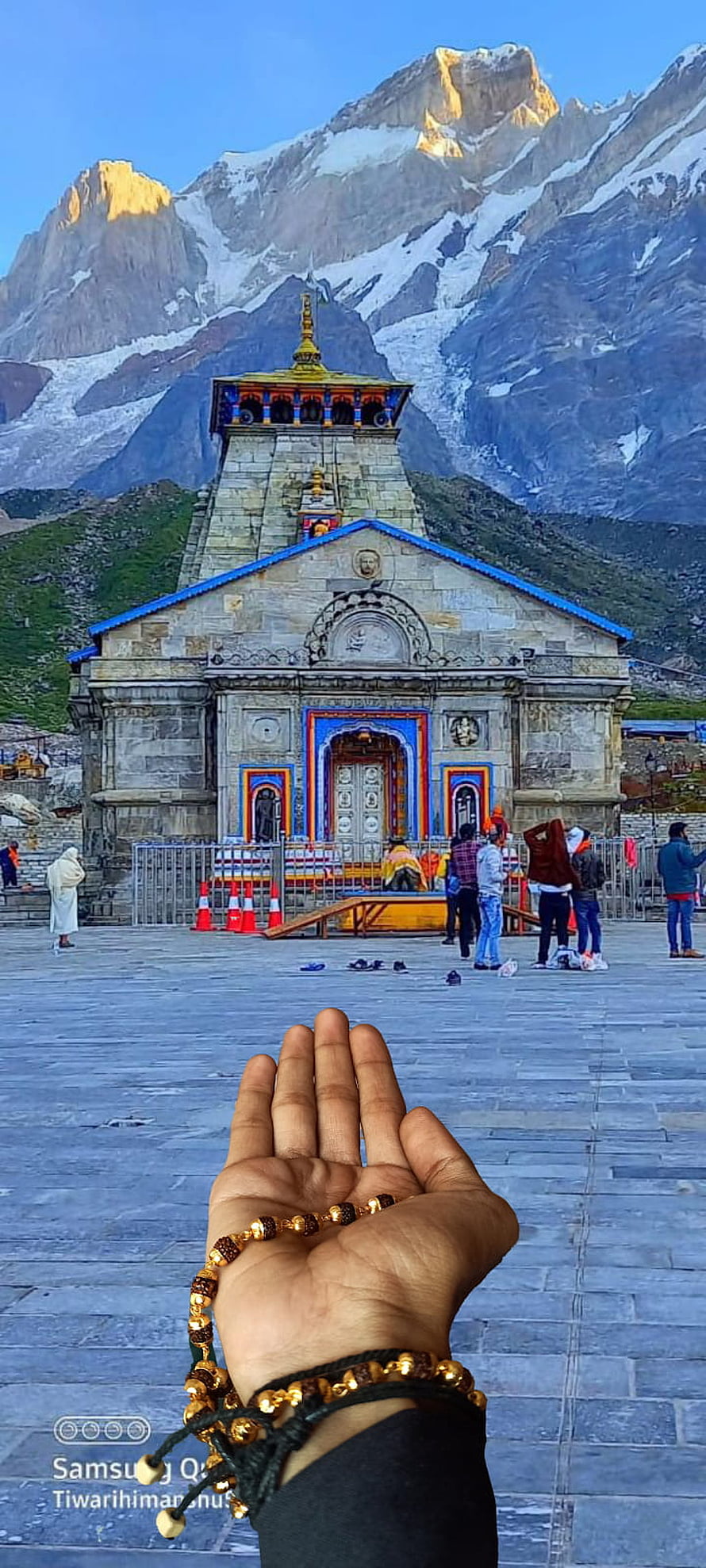 Hand holding prayer beads in front of Kedarnath Temple with snow-capped mountains HD phone wallpaper