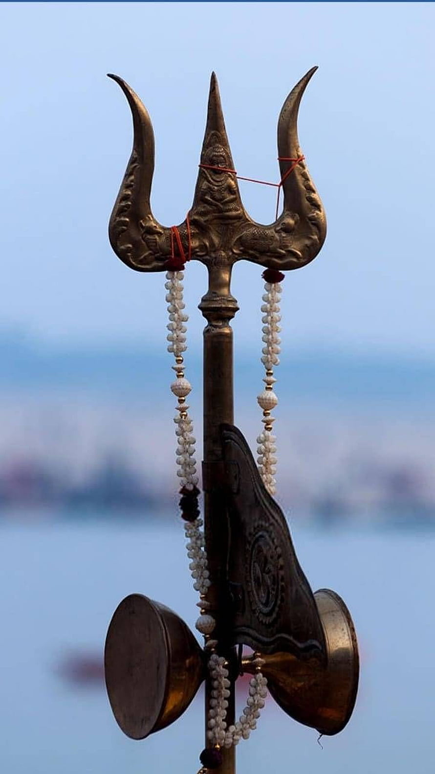 Ornate Mahadev Trishul with Rudraksha Beads and Brass Cymbals Against a Soft Blue Sky HD phone wallpaper