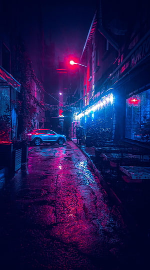 Neon-lit rainy street at night with vibrant red and blue reflections on wet pavement HD phone wallpaper