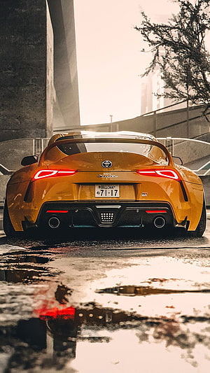 Rear View of a Yellow Toyota Supra Parked on a Wet Urban Street with Puddle Reflections HD phone wallpaper
