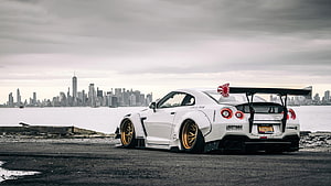 White Nissan GT-R with gold wheels parked on waterfront with New York City skyline in background HD wallpaper
