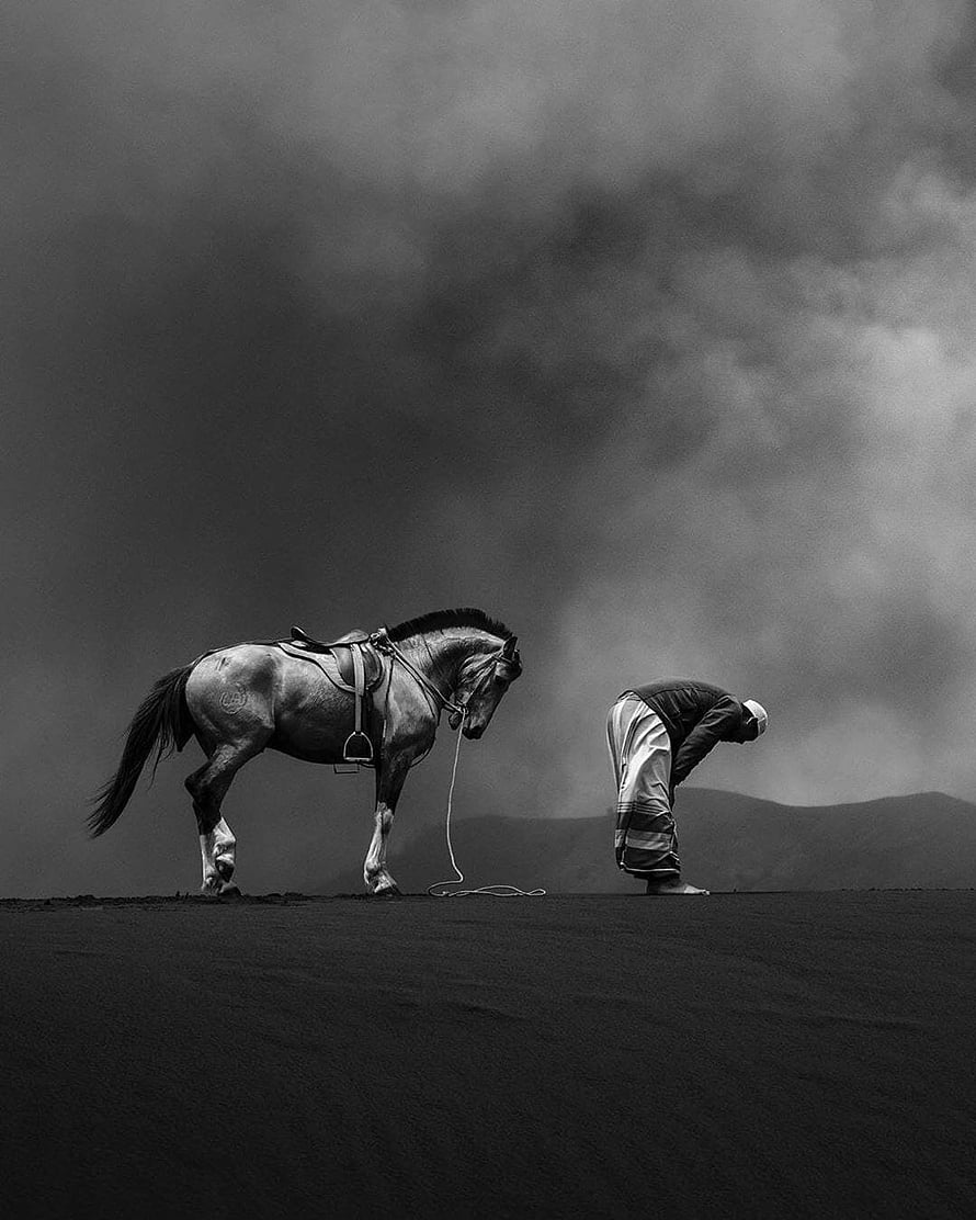 Samir Latif Black and White Photograph of a Man Praying Beside a Saddle Horse Under a Dramatic Sky, Samir Latif, horse and man praying HD phone wallpaper
