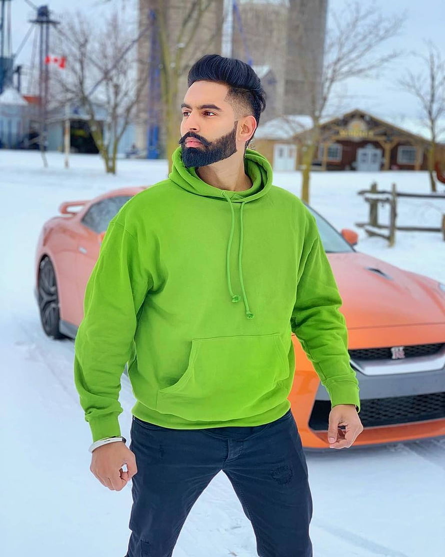 Parmish Verma in a bright green hoodie standing in the snow beside an orange sports car HD phone wallpaper