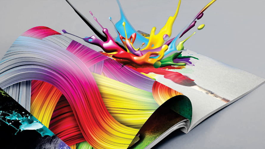Vibrant Paint Splashes Bursting from an Open Magazine on a Gray Surface HD wallpaper
