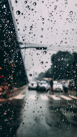 Raindrops on a car window with a blurred city street and overcast sky in the background HD phone wallpaper