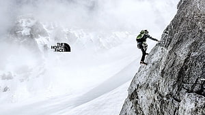 The North Face Rock Climber Scaling Snowy Mountain Cliff in Misty Alpine Landscape HD wallpaper