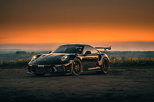 Black Porsche 911 GT3 RS parked on a dirt road at sunset with orange sky HD wallpaper