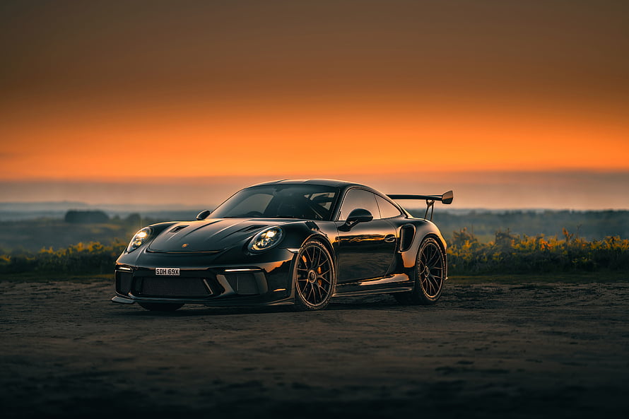Black Porsche 911 GT3 RS parked on a dirt road at sunset with orange sky HD wallpaper