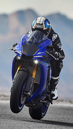 Rider on a Blue Yamaha R15 V4 Sportbike Performing a Wheelie on a Mountain Road HD phone wallpaper