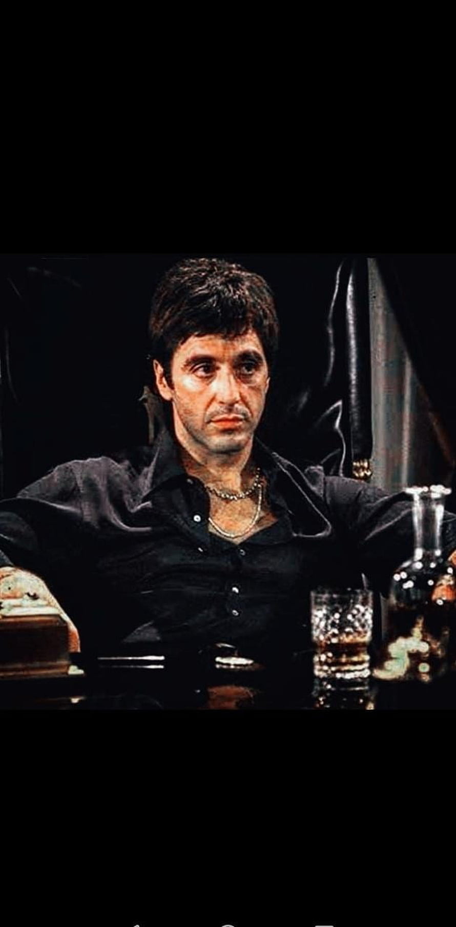 Tony Montana in a black shirt seated at a table with a whiskey glass and decanter in a dimly lit room HD phone wallpaper