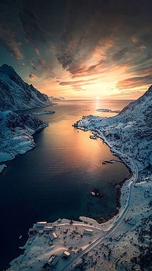 Aerial View of Snowy Fjord at Sunset with Golden Sky and Coastal Road HD phone wallpaper