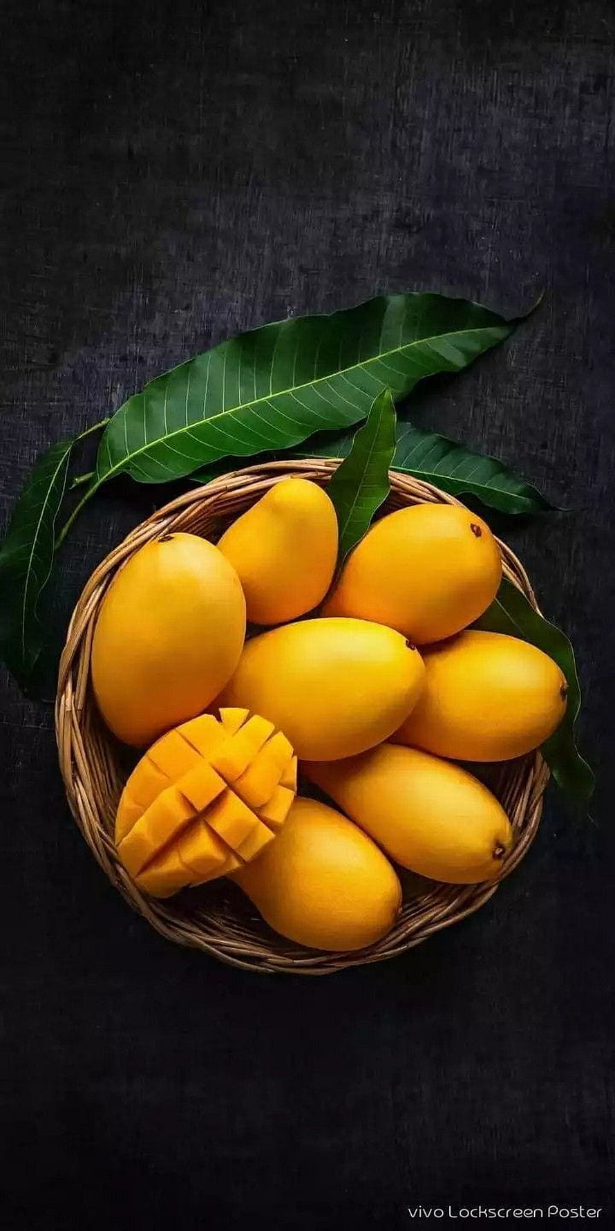 Fresh ripe mangoes in a woven basket with green leaves on a dark textured background HD phone wallpaper
