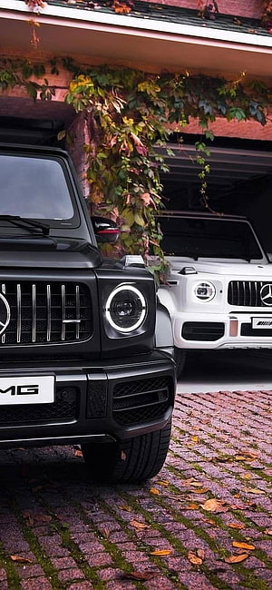 Black and White Mercedes-AMG G-Class SUVs Parked on Cobblestone Driveway HD phone wallpaper