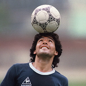 Diego Maradona Balancing a Classic Soccer Ball on His Head in a Le Coq Sportif Training Shirt HD wallpaper