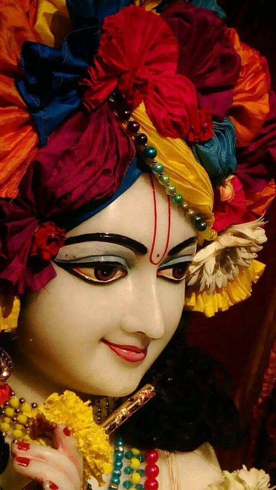 Close-up of Lord Krishna idol with colorful turban, peacock feather, and flute HD phone wallpaper