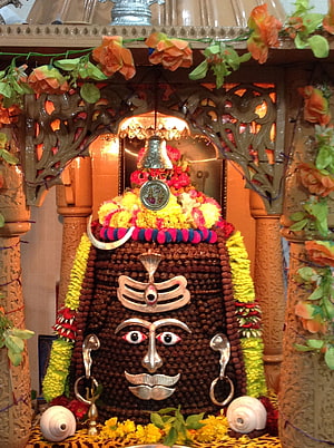 Elaborate Shiva Linga adorned with marigold garlands, silver ornaments, and a hanging bell in a decorated shrine HD phone wallpaper