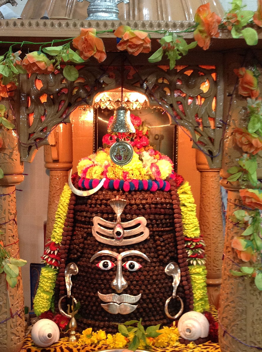 Elaborate Shiva Linga adorned with marigold garlands, silver ornaments, and a hanging bell in a decorated shrine HD phone wallpaper
