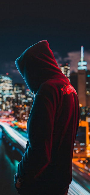 Mysterious Hooded Figure Overlooking Neon City Skyline at Night HD phone wallpaper
