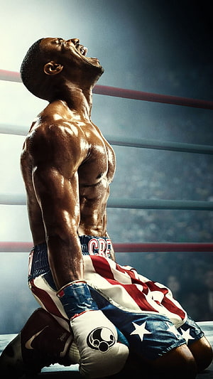 Rocky Balboa kneeling in boxing ring with American flag shorts and triumphant expression HD phone wallpaper