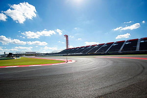Sweeping asphalt curve at a modern motorsport circuit with grandstands and a control tower under a bright blue sky HD wallpaper
