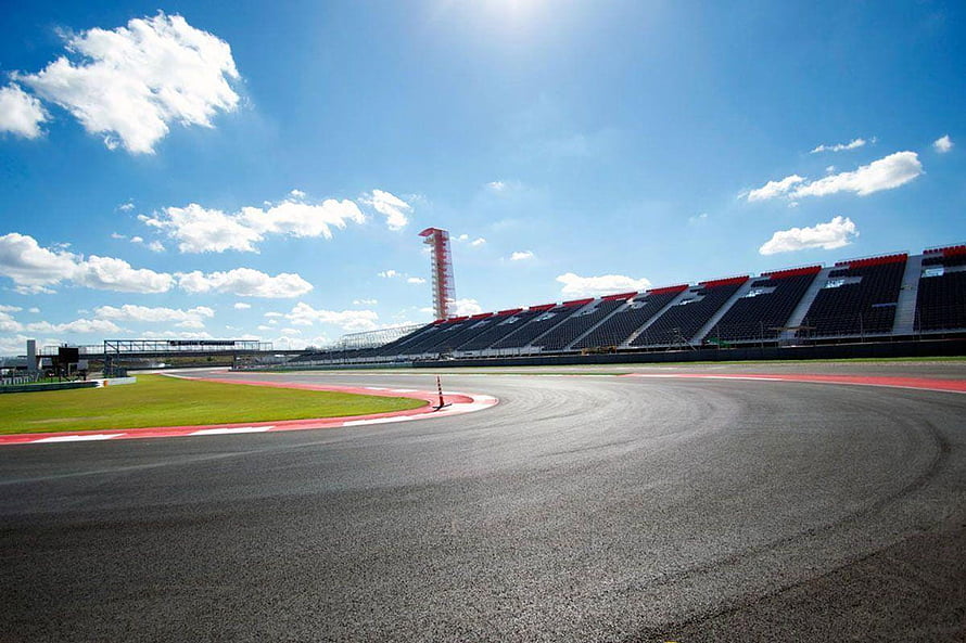 Sweeping asphalt curve at a modern motorsport circuit with grandstands and a control tower under a bright blue sky HD wallpaper