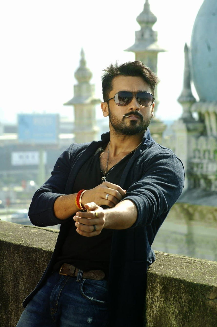 Actor Suriya wearing sunglasses and a blue shirt posing outdoors with architectural spires in the background HD phone wallpaper