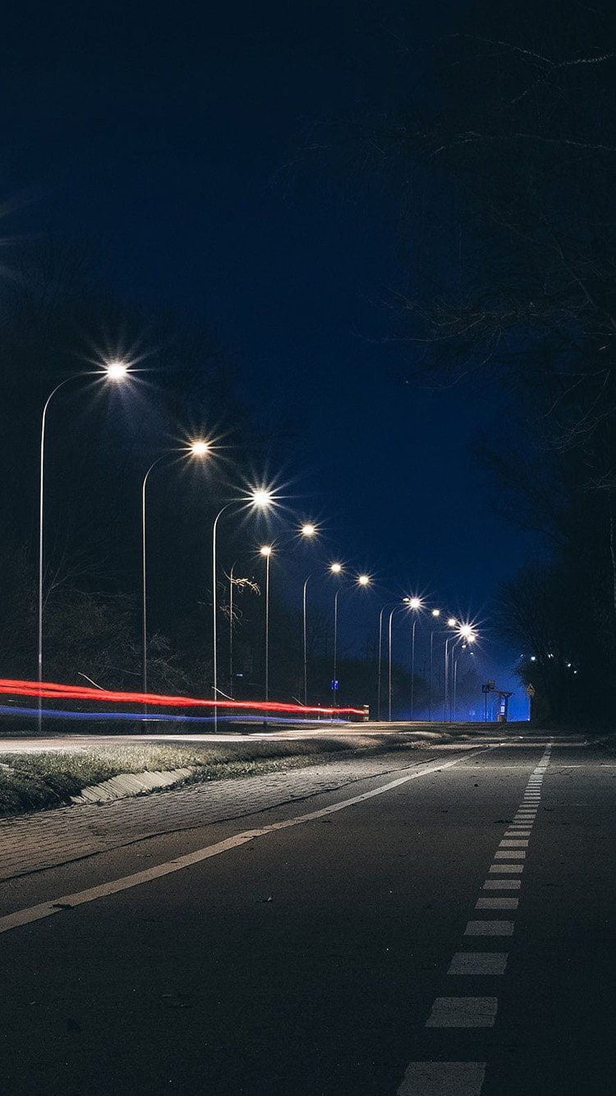 Nighttime street scene with glowing streetlights and red light trails on a dark road HD phone wallpaper