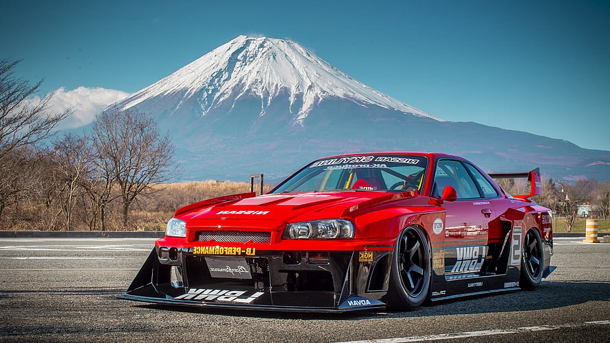 Red Nissan Skyline R34 with Liberty Walk widebody kit parked on a track with Mount Fuji in the background HD wallpaper