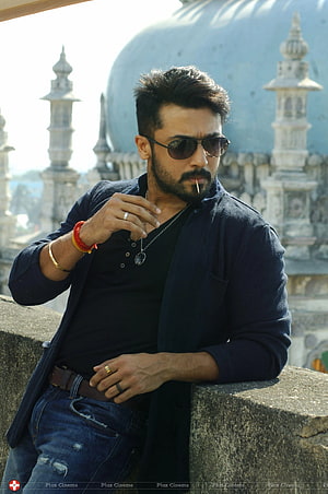 Suriya in dark casual wear with sunglasses and pendant necklace against ornate temple architecture HD phone wallpaper