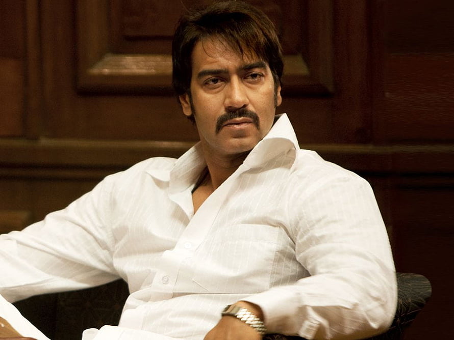 Ajay Devgn in a white shirt with a serious expression against a dark wooden background HD wallpaper