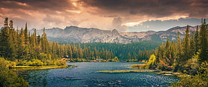 Serene Mountain Lake Surrounded by Dense Evergreen Forest Under Dramatic Clouds HD wallpaper