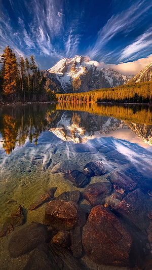 Snow-Capped Mountain Peak Reflected in a Clear Alpine Lake with Rocky Shoreline HD phone wallpaper