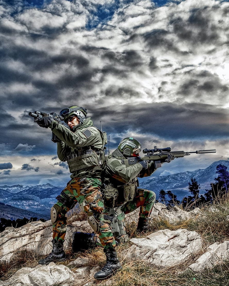 Two tactical soldiers aiming rifles on a rocky mountain ridge under a dramatic cloudy sky HD phone wallpaper