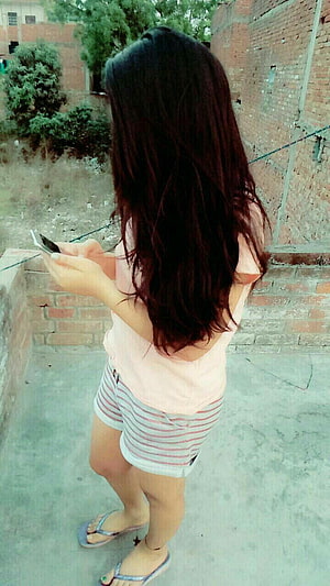 Young woman with long dark hair in pink top and striped shorts using a mobile phone outdoors, My pic, cute girl hidden face mobile HD phone wallpaper