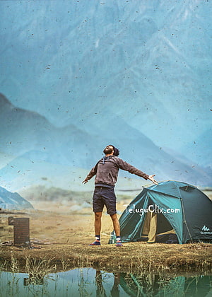 Vijay Deverakonda standing with arms outstretched beside a teal tent in a misty mountain valley HD phone wallpaper