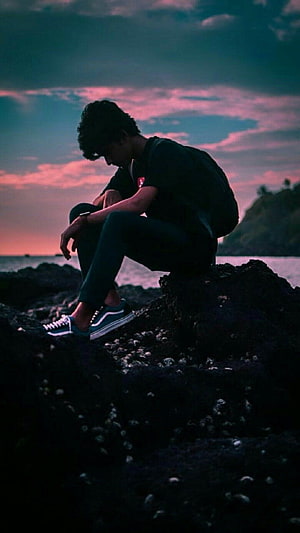 Sad Boy Sitting On Rocks By The Sea At Sunset With Pink And Blue Sky HD phone wallpaper