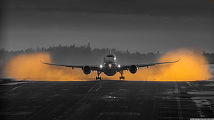 Airbus A350 Landing on Runway with Dramatic Orange Smoke and Dark Stormy Sky HD wallpaper