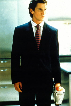 Patrick Bateman in a dark pinstripe suit holding a briefcase in a modern office setting, American Psycho's Patrick Bateman nailed 1980s businessman style, #patrick bateman HD phone wallpaper