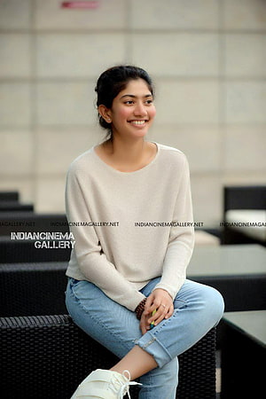 Sai Pallavi in a cream sweater and light blue jeans sitting on a wicker bench HD phone wallpaper