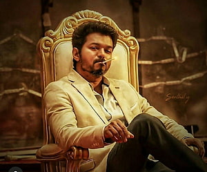 Vijay in a cream suit seated on an ornate golden throne with a cigarette HD wallpaper