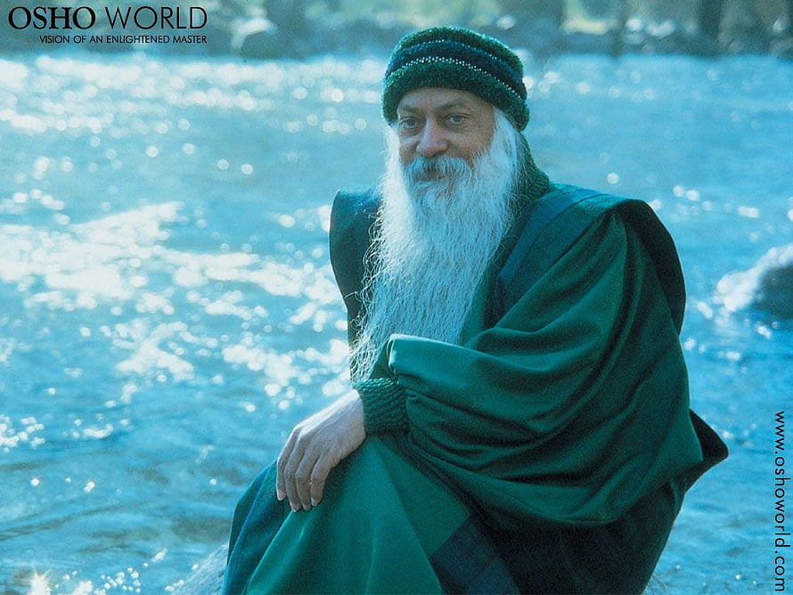 Osho sitting by a sparkling river wearing green robes and a beanie HD wallpaper