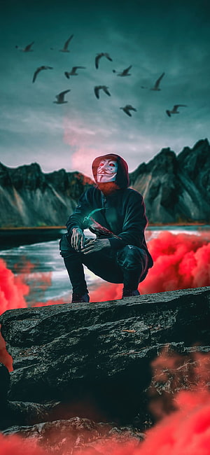 Anonymous Guy Fawkes Masked Figure Crouching on Rocky Outcrop with Red Smoke and Birds HD phone wallpaper