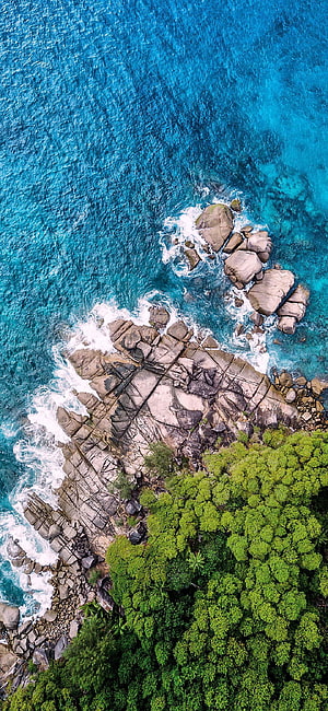 Aerial View of Turquoise Ocean Waves Crashing Against Rocky Coastline and Lush Green Forest HD phone wallpaper